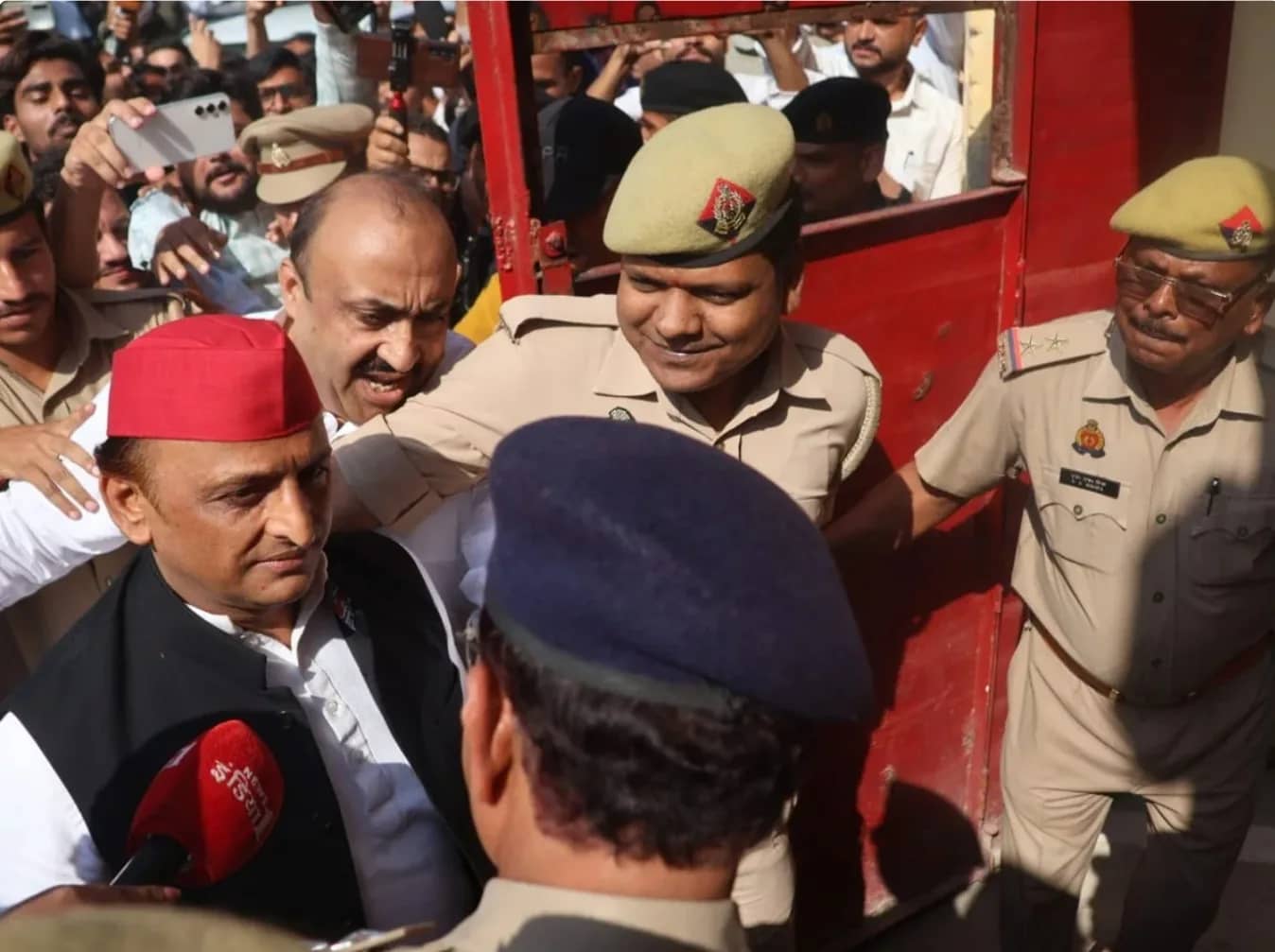 एक लाल टोपी पहने व्यक्ति को पुलिस अधिकारी और भीड़ घेरे हुए है।