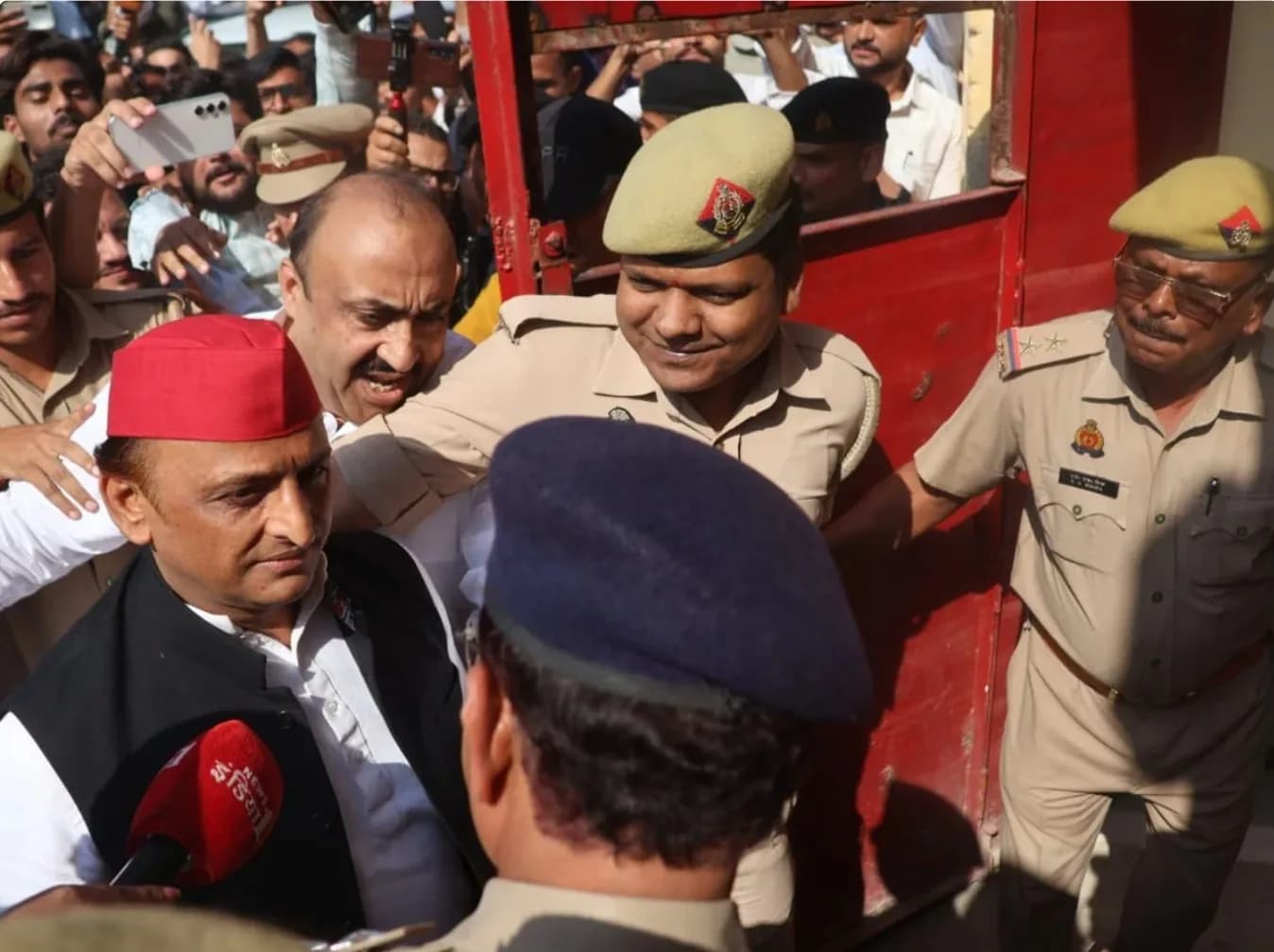 एक लाल टोपी पहने व्यक्ति को पुलिस अधिकारी और भीड़ घेरे हुए है।