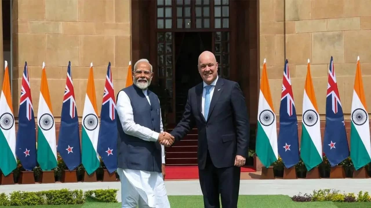 भारतीय और न्यूजीलैंड के प्रधानमंत्रियों ने झंडों के सामने हाथ मिलाया।