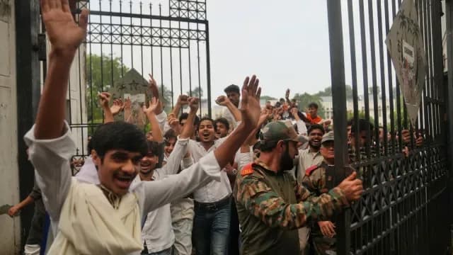 एक भीड़ एक खुले गेट से गुजर रही है, जिसमें एक व्यक्ति अपने हाथ ऊपर उठाए हुए है।