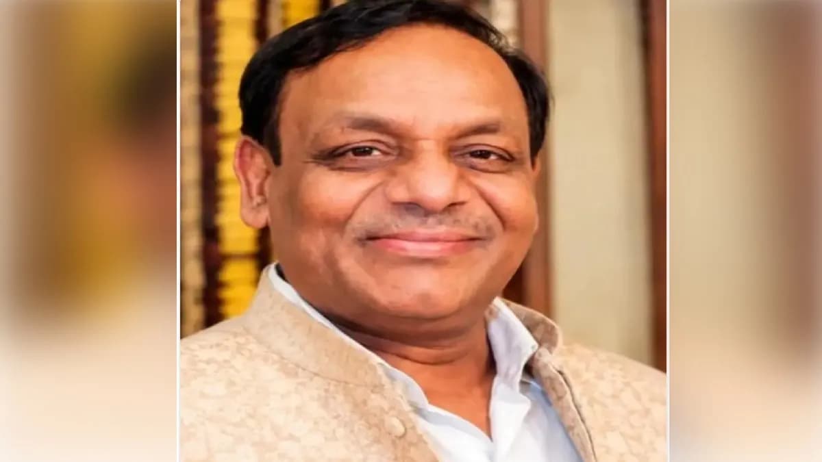 एक भारतीय व्यक्ति मुस्कुराते हुए, हल्के रंग की जैकेट और सफेद शर्ट पहने हुए।