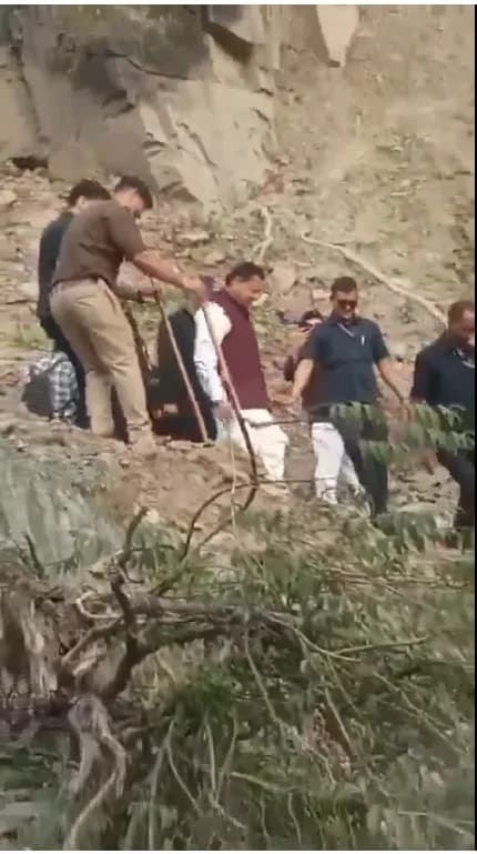एक व्यक्ति एक ढलान पर एक अन्य व्यक्ति को ऊपर खींच रहा है, जबकि अन्य लोग देख रहे हैं।