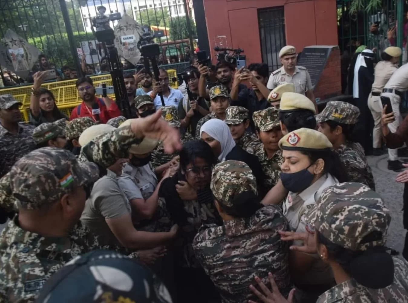 पुलिस अधिकारियों और सैन्य वर्दी पहने लोगों की भीड़ एक महिला को घेरे हुए है।