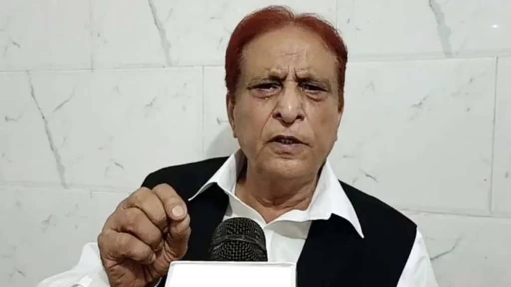 एक व्यक्ति सफेद शर्ट और काले कोट में माइक्रोफोन के सामने बोल रहा है।