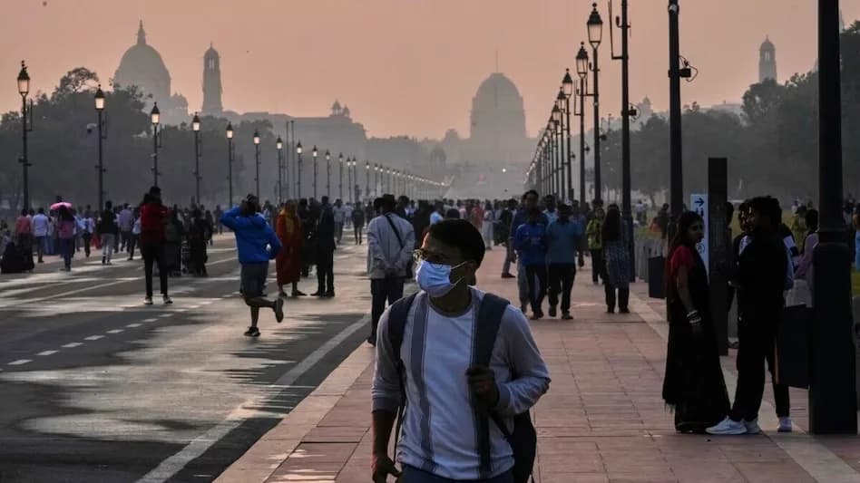 एक व्यक्ति मास्क पहने हुए सड़क पर चल रहा है, जिसके पीछे कई लोग और इमारतें हैं।